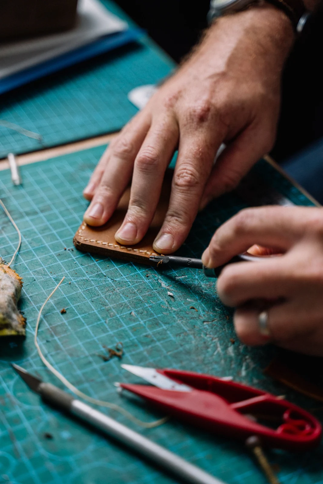 Hands working on a leather component at a cutting mat